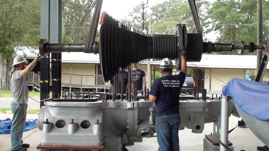 Image of Millwrights lowering large crankshaft into industrial machinery