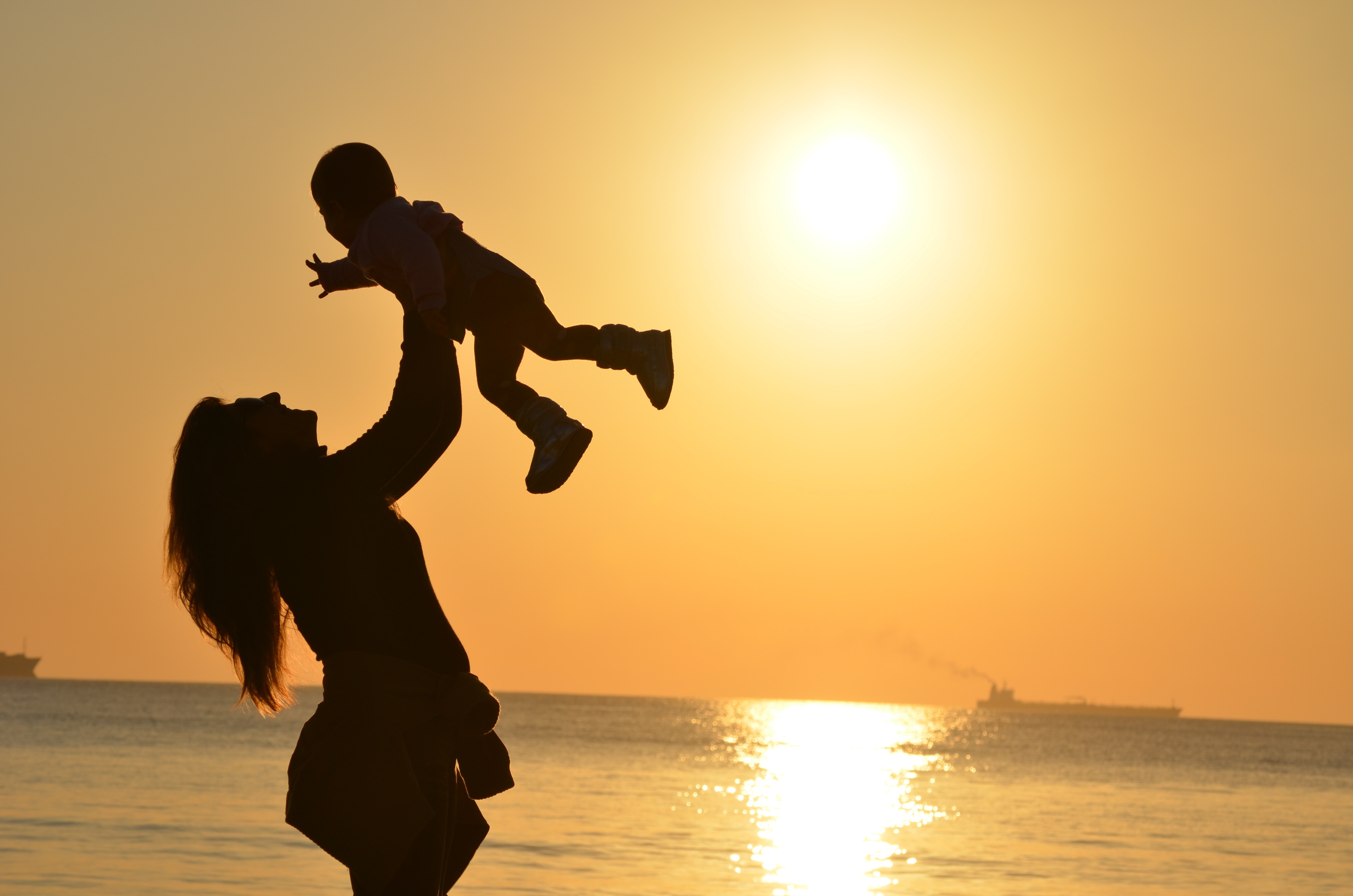 silhouette of a mother lifting a child up in the air at sunset 